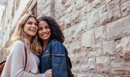 Junge Frauen stehen zusammen an einer Steinmauer. Zwei lächelnde Frauen posieren für ein Foto im Freien. - JLPSF05102
