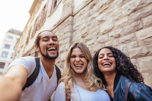 Joyful man with two women friends posing for a selfie outdoors. Friends having fun while exploring the city. - JLPSF05103