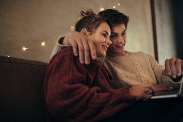 Entspannter Mann und Frau sitzen auf dem Sofa und benutzen einen Laptop. Paar mit Laptop im gemütlichen Wohnzimmer. - JLPSF05108