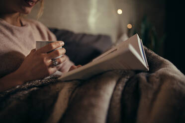 Ausgeschnittene Aufnahme einer Frau mit Buch und Kaffee, die nachts auf dem Bett ein Buch liest. - JLPSF05135