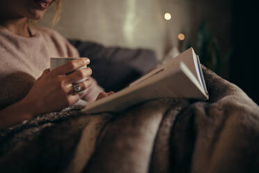 Cropped shot of female hands with book and coffee. Female reading book on bed at night. - JLPSF05135