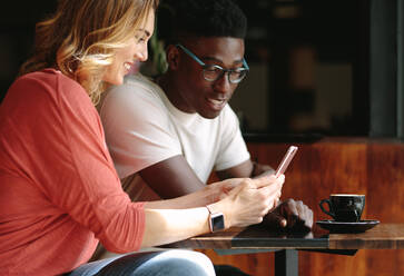 Ein Paar sitzt in einem Café und benutzt ein Handy. Ein Mann und eine Frau sitzen an einem Kaffeetisch und schauen auf ein Mobiltelefon. - JLPSF05136