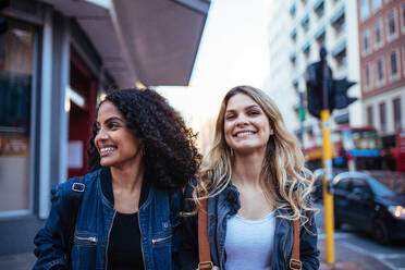 Zwei fröhliche Frauen, die auf der Straße spazieren gehen. Frauen, die mit Reisetaschen die Stadt erkunden. - JLPSF05148