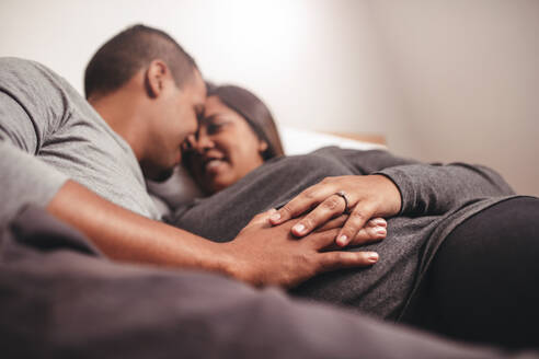Romantischer junger Mann und Frau auf dem Bett liegend, Fokus auf Hände auf dem Bauch. Afrikanisches schwangeres Paar, das ein Baby erwartet. - JLPSF05151