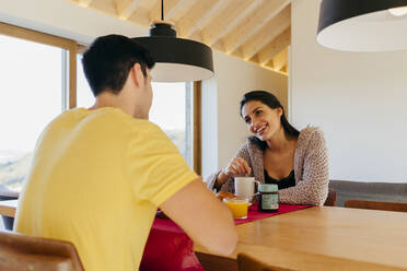 Attractive Hispanic happy lady and young guy having breakfast together at table in modern kitchen - ADSF39369