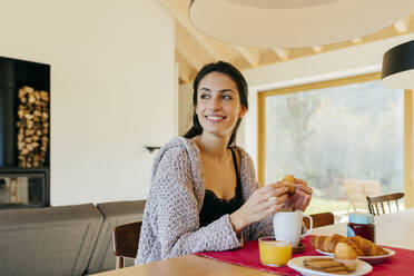 Attractive Hispanic lady sitting at table and having breakfast in modern house - ADSF39371