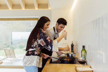 Seitenansicht einer attraktiven hispanischen jungen Frau und eines jungen Mannes, die zusammen in der Küche kochen - ADSF39390