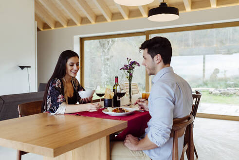 Seitenansicht eines fröhlichen attraktiven Paares beim Essen am Küchentisch - ADSF39395