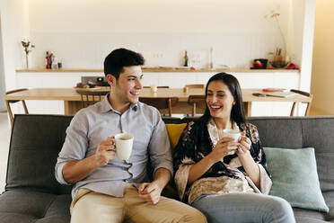 Cheerful attractive couple with mug sitting on settee near kitchen - ADSF39397