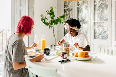 Junge multiethnische Frauen sitzen am Tisch und essen gesundes Essen beim Frühstück am sonnigen Morgen in einer modernen Wohnung - ADSF39407