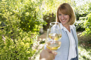 Lächelnde Frau stößt im Garten mit Wein an - SVKF00621