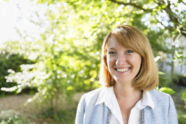 Smiling mature businesswoman in redhead standing in garden - SVKF00623