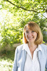 Happy businesswoman in redhead standing in garden - SVKF00624