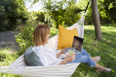 Freiberufler sitzt mit Laptop in Hängematte im Garten - SVKF00630