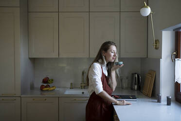 Woman with eyes closed smelling from bowl standing at kitchen counter - NJAF00033
