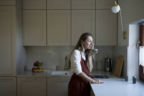 Frau mit geschlossenen Augen riecht aus einer Schüssel am Küchentisch - NJAF00033