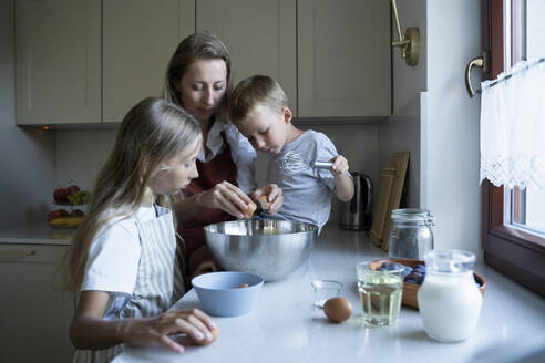 Mutter und Kinder bereiten Kuchen in der Küche zu Hause vor - NJAF00034