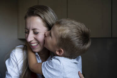 Boy kissing happy mother in kitchen - NJAF00040