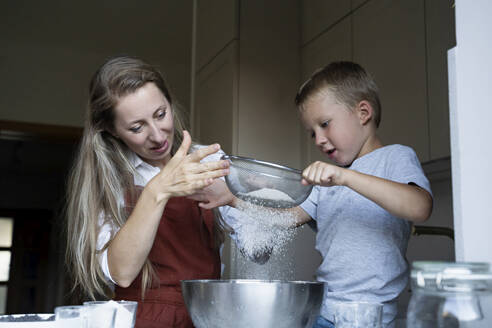Mutter und Sohn sieben Mehl für die Zubereitung von Kuchen zu Hause - NJAF00042