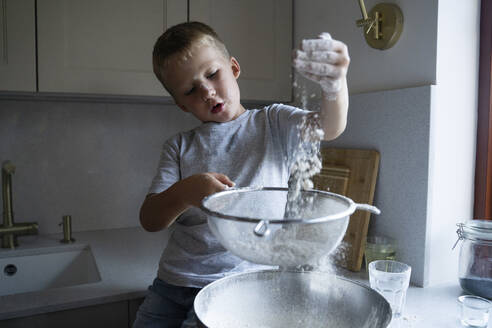 Niedlicher Junge siebt Mehl für die Zubereitung von Kuchen zu Hause - NJAF00043