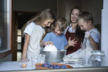 Glückliche Kinder bei der Zubereitung von Teig durch die Mutter in der Küche zu Hause - NJAF00046