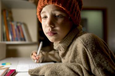Boy wearing sweater and knit hat studying at home - ANAF00159