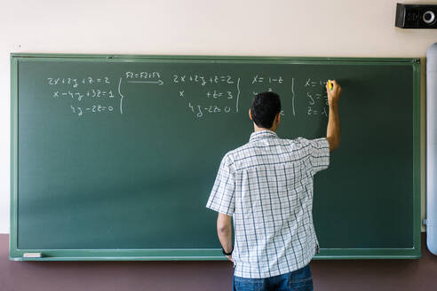 Mathelehrer schreibt Formeln an die Tafel im Klassenzimmer - DAMF01092