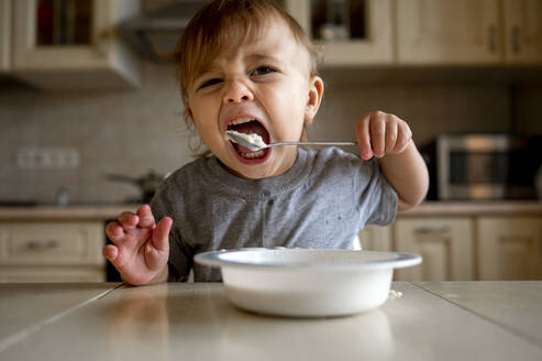 Kleiner Junge isst Brei mit Löffel in der Küche - ANAF00163