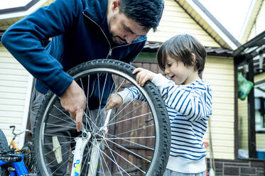 Sohn hilft Vater bei der Reparatur von Fahrradrädern vor dem Haus - ANAF00167