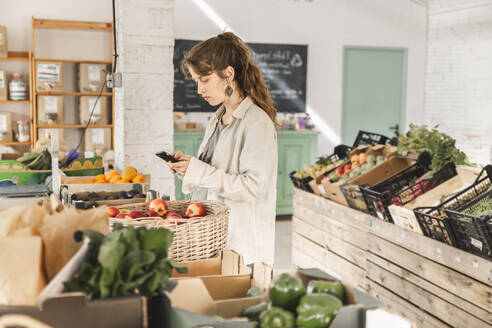 Customer using smart phone standing in vegetable store - PCLF00136