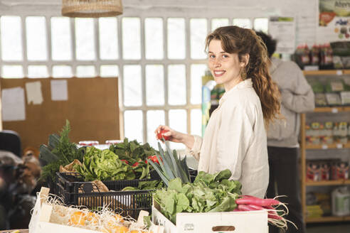 Smiling woman buying vegetables from greengrocer shop - PCLF00144