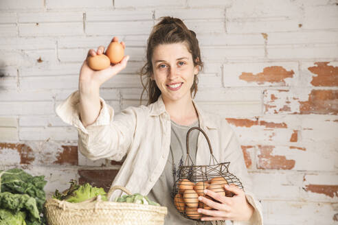 Smiling grocer showing eggs in front of brick wall - PCLF00154