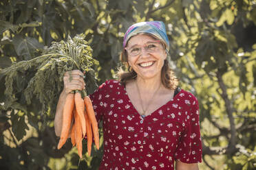 Happy woman holding bunch of fresh carrots in farm - PCLF00171