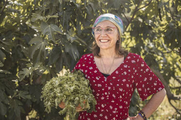 Thoughtful woman with fresh arugula in front of plants at farm - PCLF00172