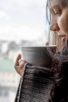 Frau in Decke eingewickelt mit Kaffeetasse zu Hause - ANAF00177