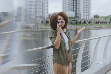 Smiling young woman talking through mobile phone standing by railing - YTF00210