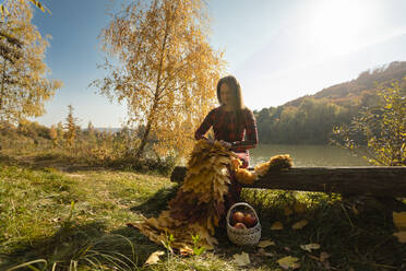 Frau mit gelben Blättern strickt Schal auf Baumstamm im Park - OSF01065