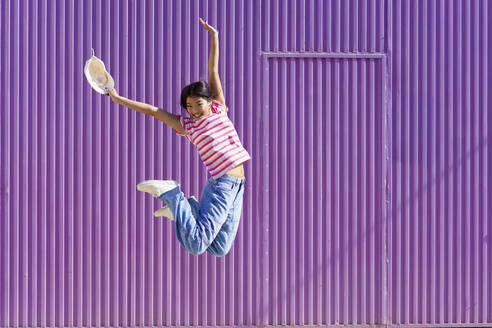 Cheerful woman jumping in front of purple background - JSMF02432