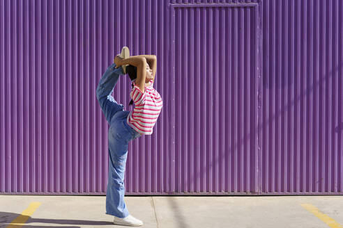 Young woman doing stretching exercise in front of corrugated wall - JSMF02433