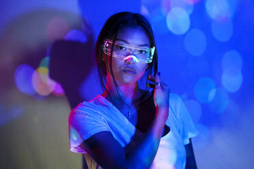 Confident young woman wearing smart glasses in front of wall - JSMF02442