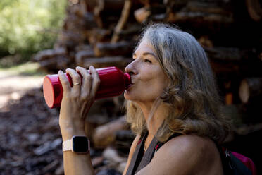 Woman with gray hair drinking water through bottle - FLLF00779