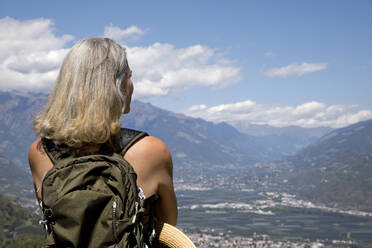 Ältere Frau mit grauen Haaren betrachtet die Landschaft an einem sonnigen Tag - FLLF00786
