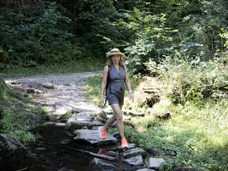 Lächelnde ältere Frau mit Hut, die auf Felsen im Wald läuft - FLLF00790