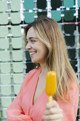 Happy woman showing ice cream in front of glass wall - SEAF01313