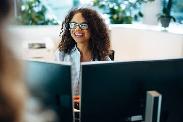 Smiling woman working at front desk of a municipality office. Female administrator sitting behind the desk looking at a woman and smiling. - JLPSF05161