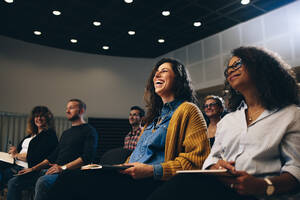 Geschäftsfrau, die während einer Firmenveranstaltung im Publikum sitzt und lacht. Geschäftsleute, die während eines Seminars lächeln. - JLPSF05175