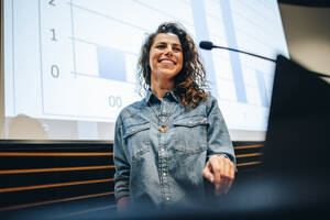 Erfolgreicher Geschäftsmann, der eine Präsentation während eines Gipfels hält. Eine weibliche Rednerin steht am Podium und lächelt bei einem Seminar. - JLPSF05182