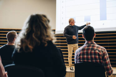 Ein Geschäftsmann zeigt auf eine Projektionsfläche und hält eine Präsentation für das Publikum in einem Kongresszentrum. Ein hochrangiger Redner hält eine Präsentation auf einem Gipfel. - JLPSF05183