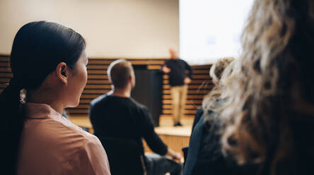 Rückansicht eines Menschen, der bei einer Firmenveranstaltung im Publikum sitzt. Weibliche Fachkraft sitzt in einem Seminar und hört der Rede zu. - JLPSF05271