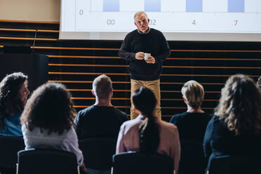 Älterer Geschäftsmann, der eine motivierende Rede vor Geschäftsleuten hält, die in einem Kongresszentrum sitzen. - JLPSF05272